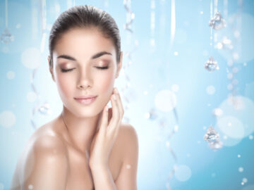 Close-up portrait of a beautiful young brunette holding hand by face with eyes closed on blue background.